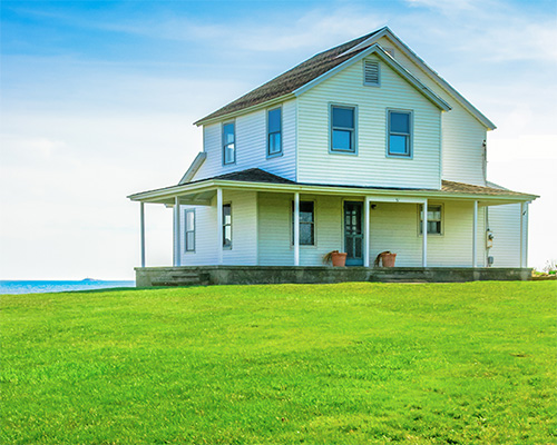 White farmhouse with pristine green lawn on a sunny day, illustrating residential lawn protection and curb appeal