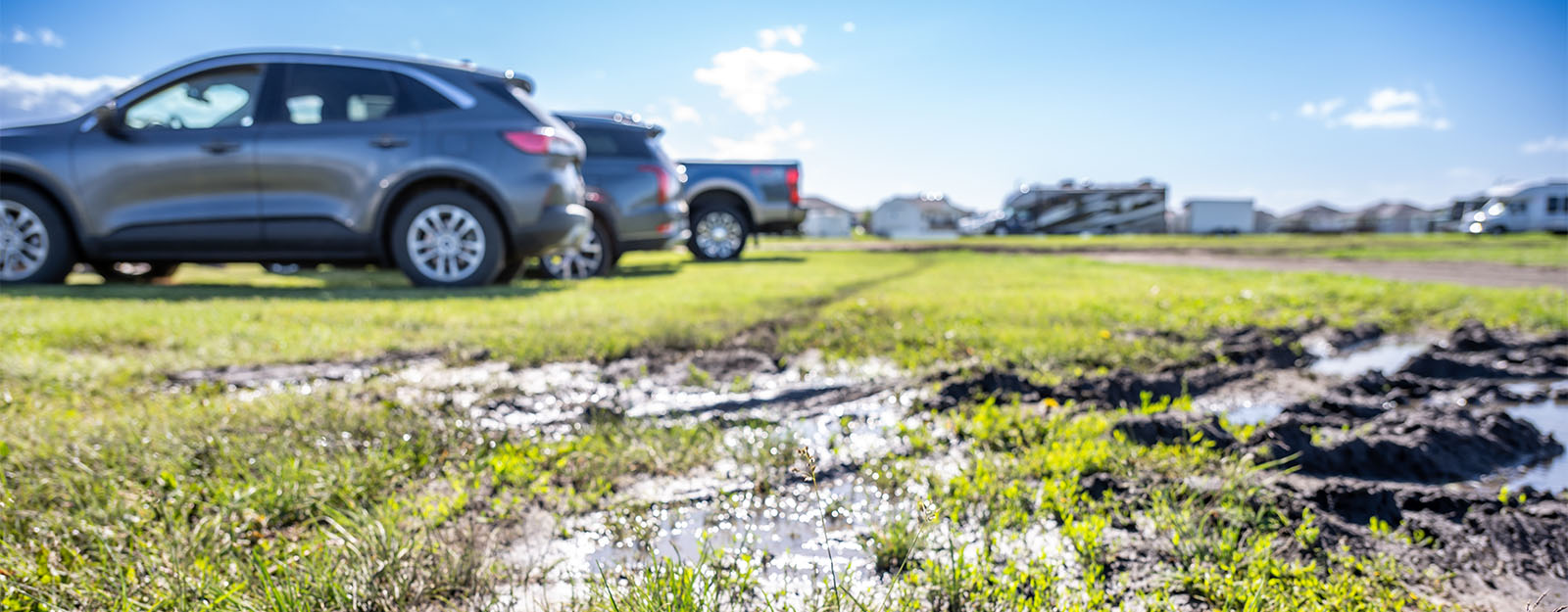 Two cars parked on muddy, damaged grass showing the problem of unprotected overflow parking on soft ground