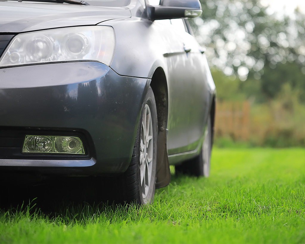 Car parked on a reinforced green grass parking area, showing Tenax turf reinforcement mesh installed result