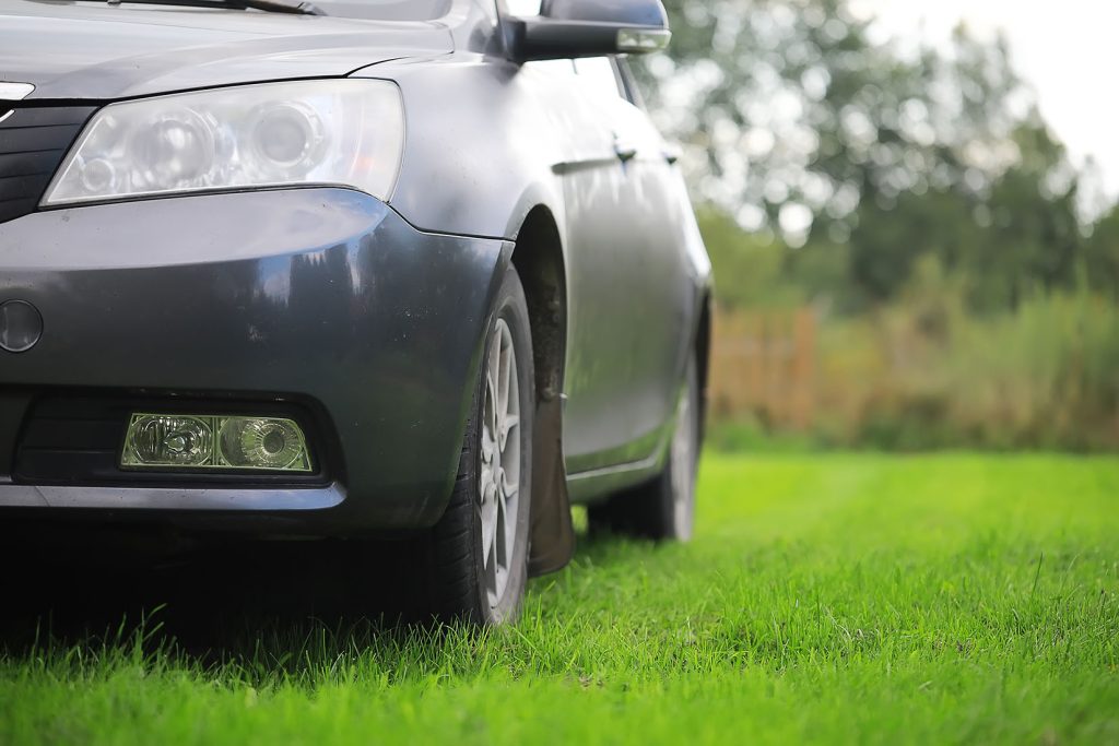 Car parked on a reinforced green grass parking area, showing Tenax turf reinforcement mesh installed result