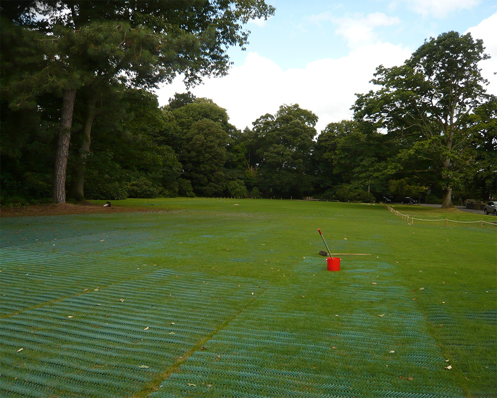 Wide landscape view of Tenax GP Flex ground protection mesh installed across a large event or park field with a building visible in background