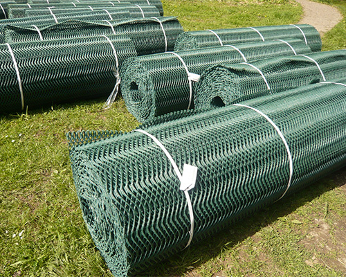 Multiple Tenax GP Flex ground protection mesh rolls stacked in a grass field ready for deployment, showing large-scale installation preparation