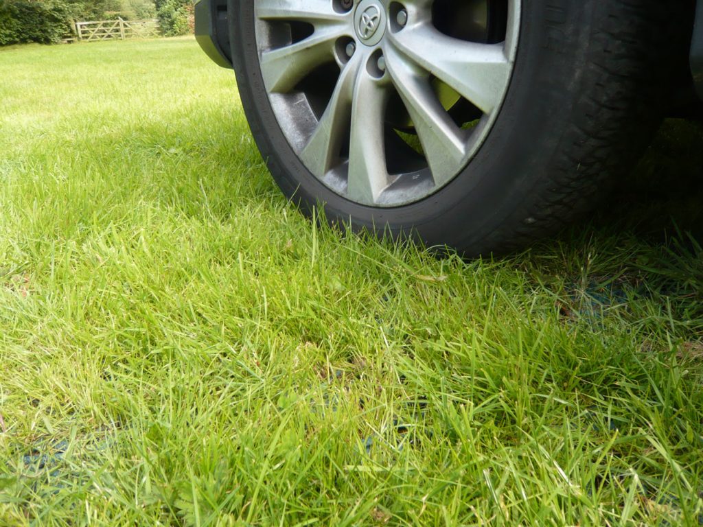 Real-world view of a car wheel on Tenax GP Flex ground protection mesh with grass visible at the vehicle edge