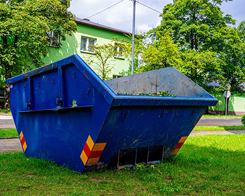 Blue skip or dumpster bin placed on a residential grass lawn during home improvement or construction work, showing the need for lawn protection during staging