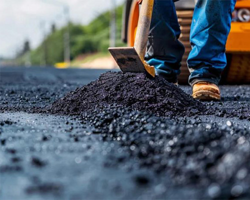 Worker laying fresh asphalt with machinery, representing conventional hard paving as an alternative to permeable grass reinforcement mesh