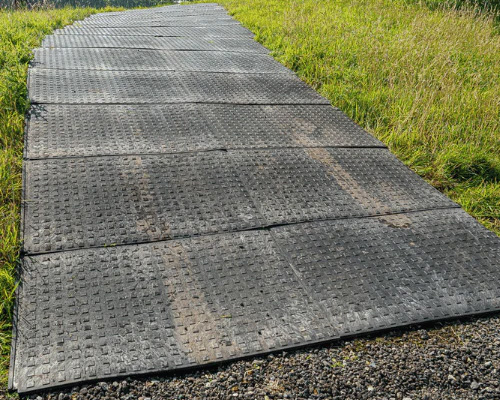 Dark grey rubber access mats laid on grass as a comparison alternative to Tenax heavy-duty ground protection mats for construction and events