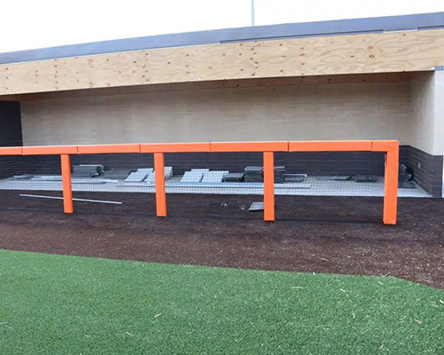 Temporary orange metal barrier fencing at an event or sports facility, shown as a comparison alternative to Tenax grass parking mesh for crowd and ground management