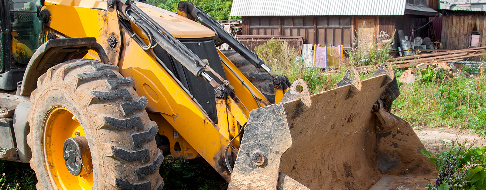 Orange front-end loader clearing tree debris from a residential lawn during construction or landscaping work, showing the need for ground protection during heavy equipment use