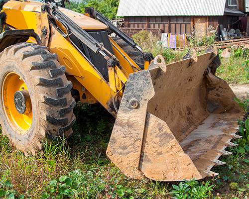 Orange front-end loader clearing tree debris from a residential lawn during construction or landscaping work, showing the need for ground protection during heavy equipment use