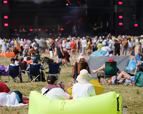 Large crowd at an outdoor music festival seated on grass with stage lighting at night, showing the scale of event ground traffic that Tenax grass protection mesh manages