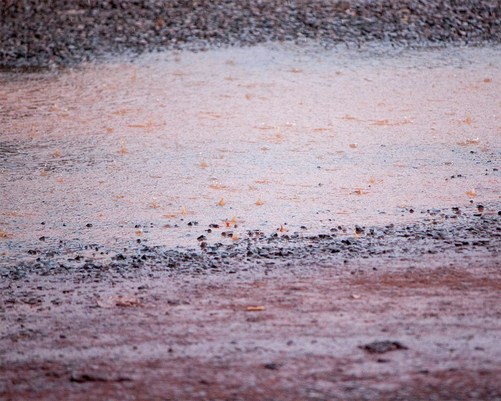 rain falls on muddy parking lot puddle