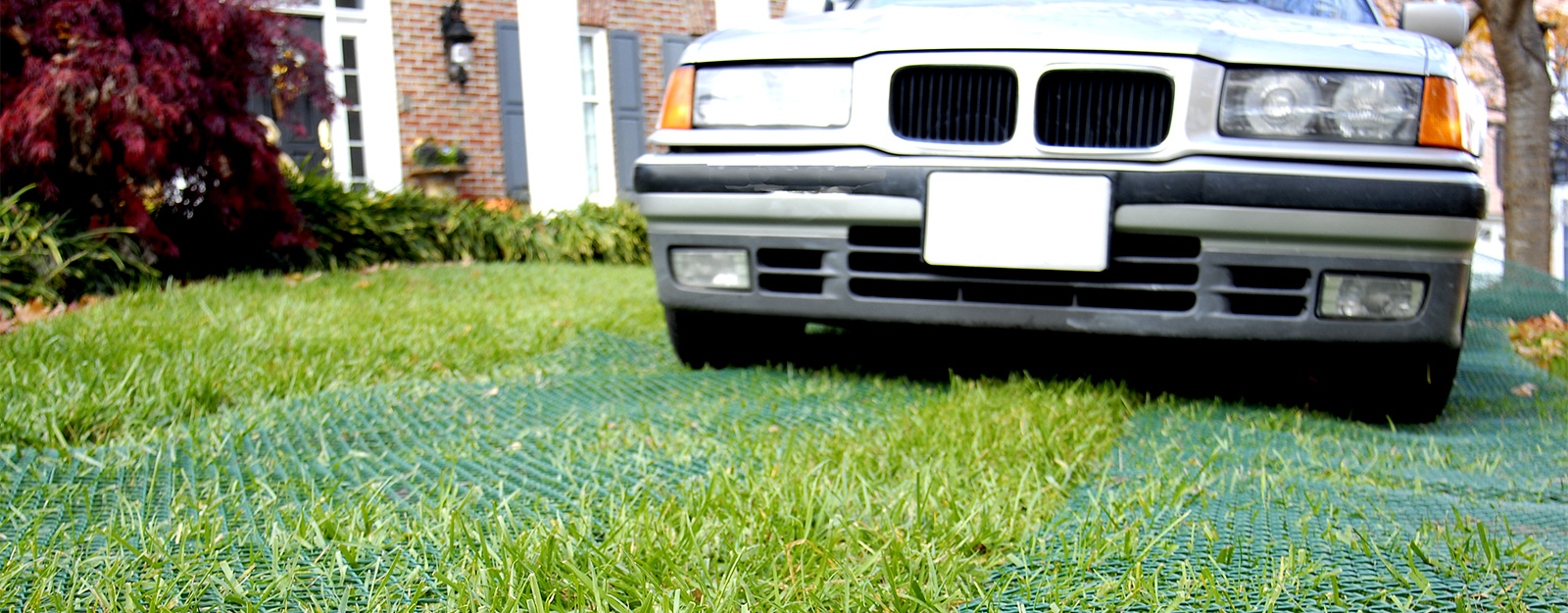 Car parked on a sunny reinforced green grass surface, showing Tenax ground protection mesh installed result