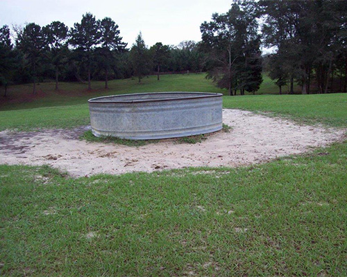 Livestock water station on bare sandy ground before Tenax mesh installation, showing unprotected farm ground