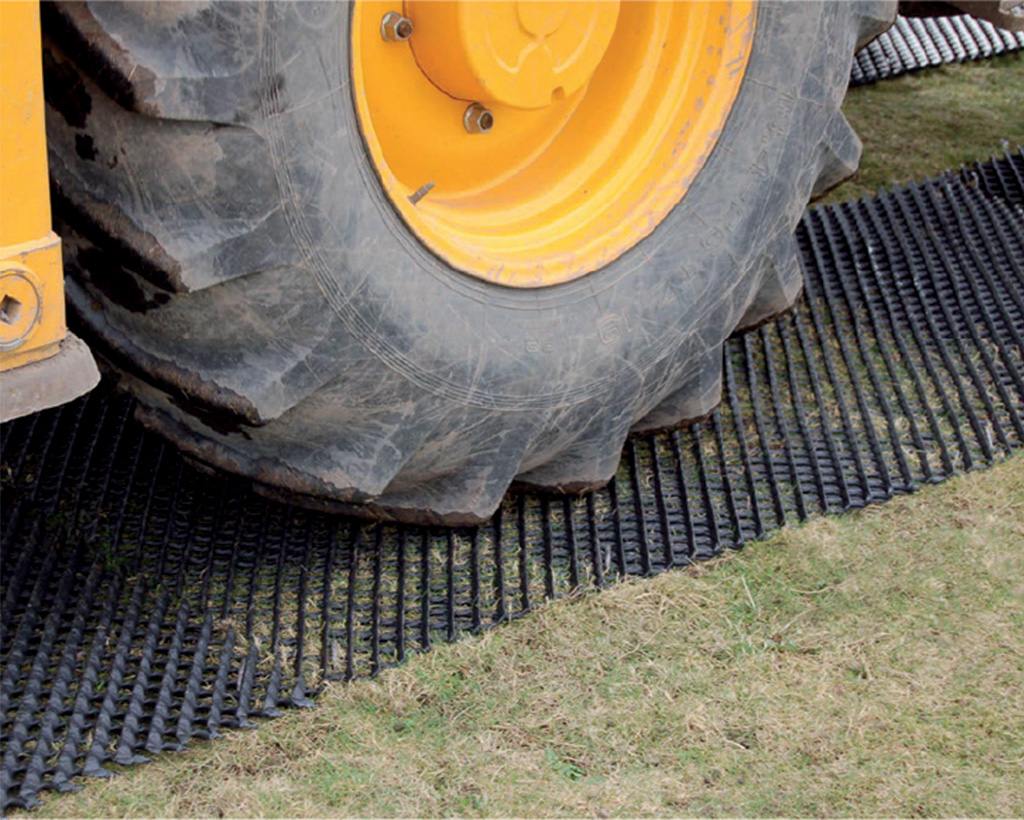 Large tractor wheel on a Tenax Trackway ground protection mat, showing heavy agricultural or construction vehicle use