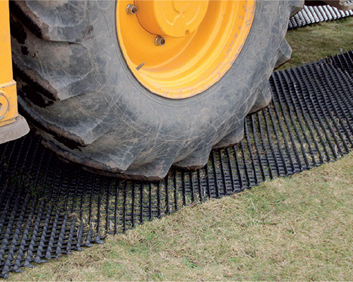 Large tractor wheel on a Tenax Trackway ground protection mat, showing heavy agricultural or construction vehicle use