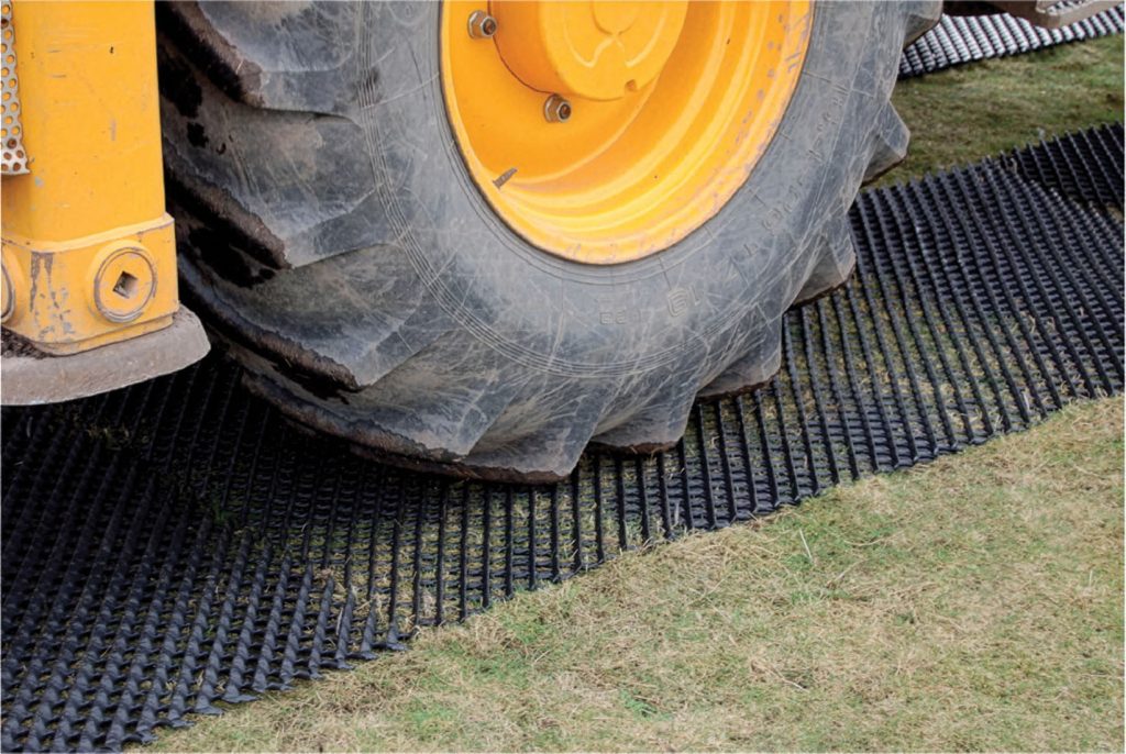 Large tractor wheel on a Tenax Trackway ground protection mat, showing heavy agricultural or construction vehicle use