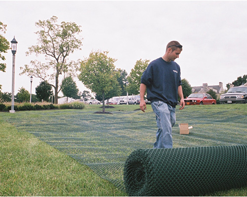 Man unrolling Tenax ground protection mesh across green grass during an outdoor installation