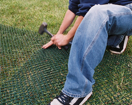 Man kneeling to install and pin Tenax ground protection mesh to the ground during a DIY or professional installation