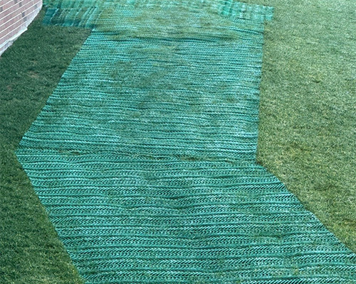 Straight run of Tenax GP Flex ground protection mesh on a stadium berm alongside a concrete walkway